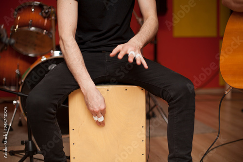 Percussionist playing cajon on a rehearsal studio with drums and music stuff on the background photo