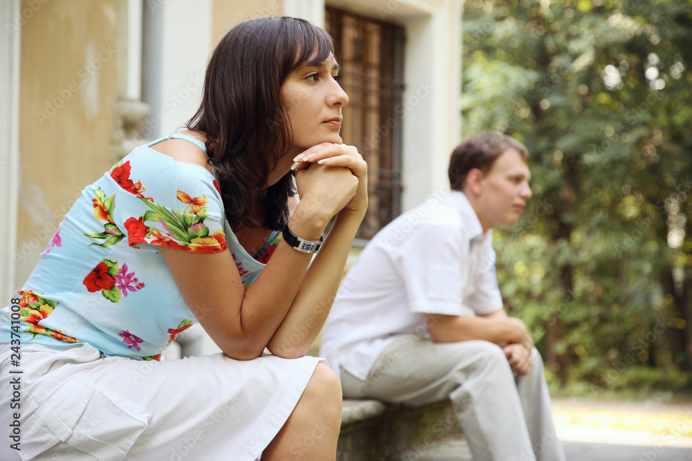 Young sad woman and man sitting on marble steps in park, selective focus