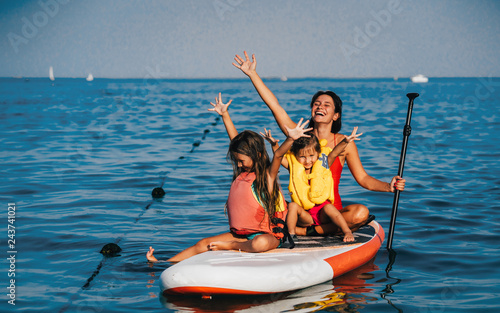 Mother with two daughters stand up on a paddle board