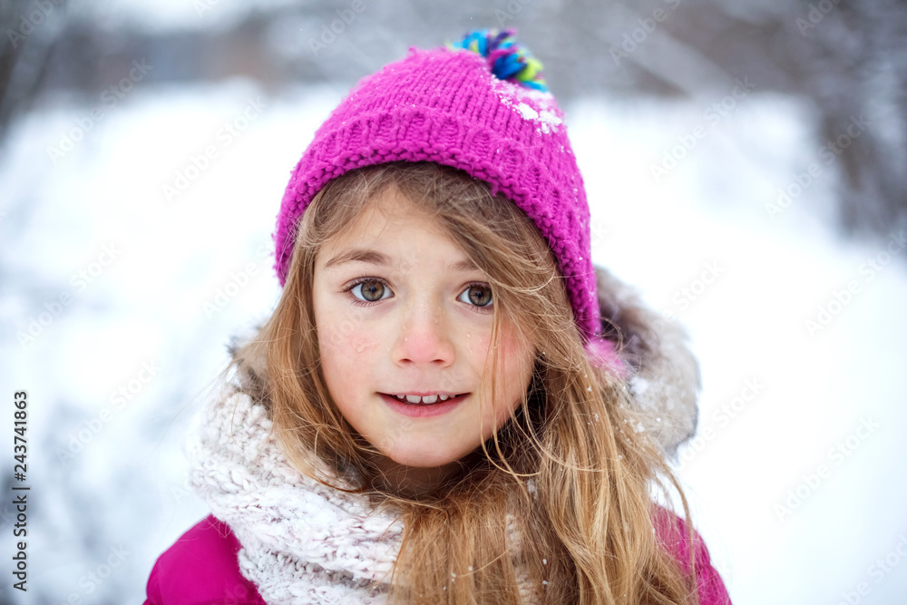 Beautiful young girl wearing pink jacket and knitted hat playing with snow in winter park. Child walking in snowy forest. Family vacation with kid in mountains Beautiful young girl wearing pink jacket and knitted hat playing with snow in winter park. Child walking in snowy forest. Family vacation with kid in mountains