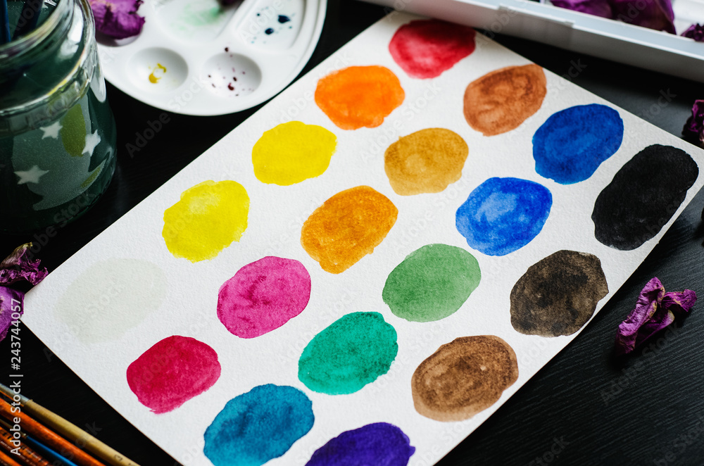 Watercolor spots on the paper, palette and dry petals on black background Watercolor spots on the paper, palette and dry petals on black background