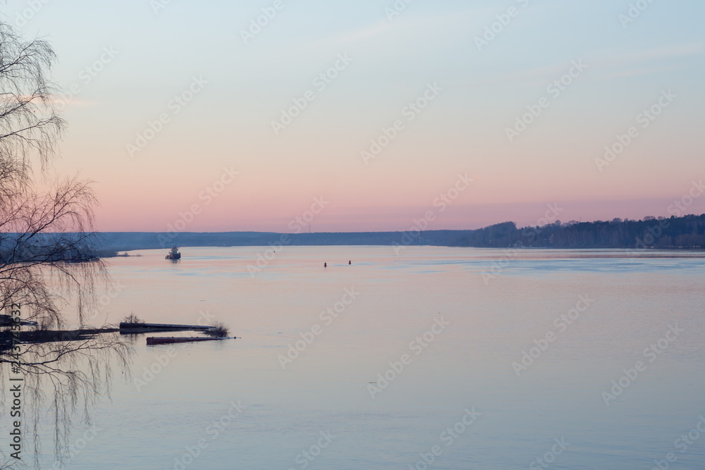 Peaceful spring landscape at sunset on the river with ship and forest in the background.