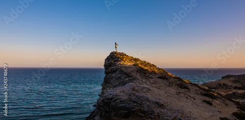 Persona subida en una montaña frente al mar al atardecer 