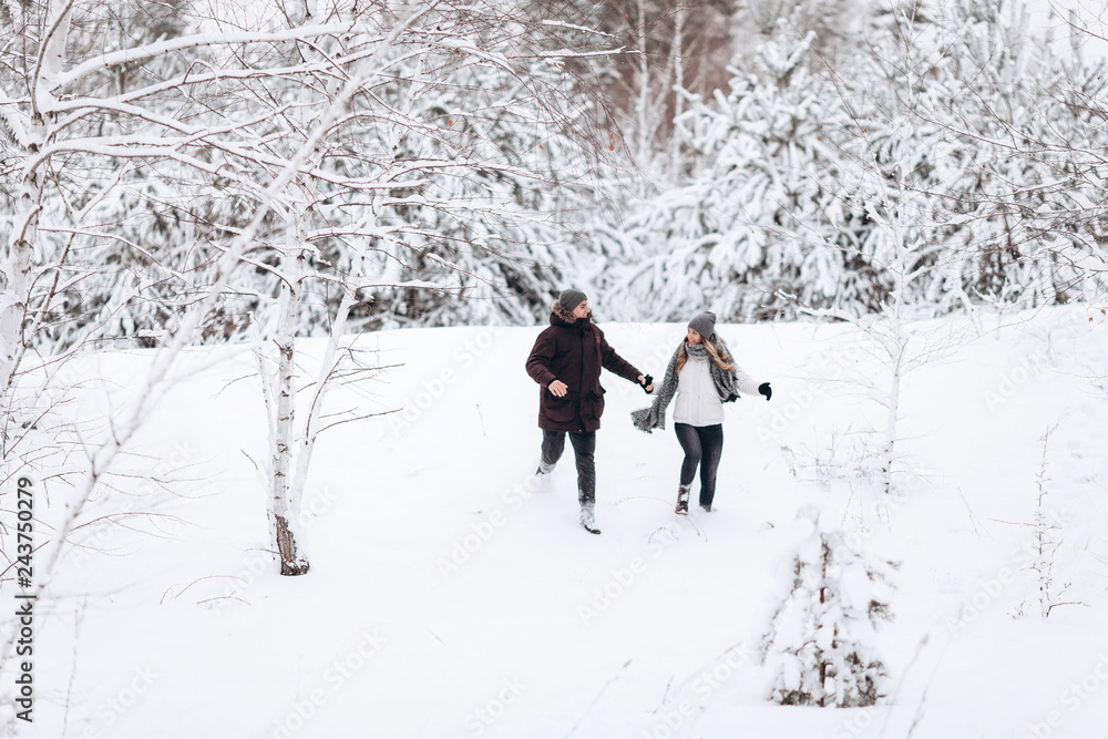 Young couple running on a snowy winter field near pine