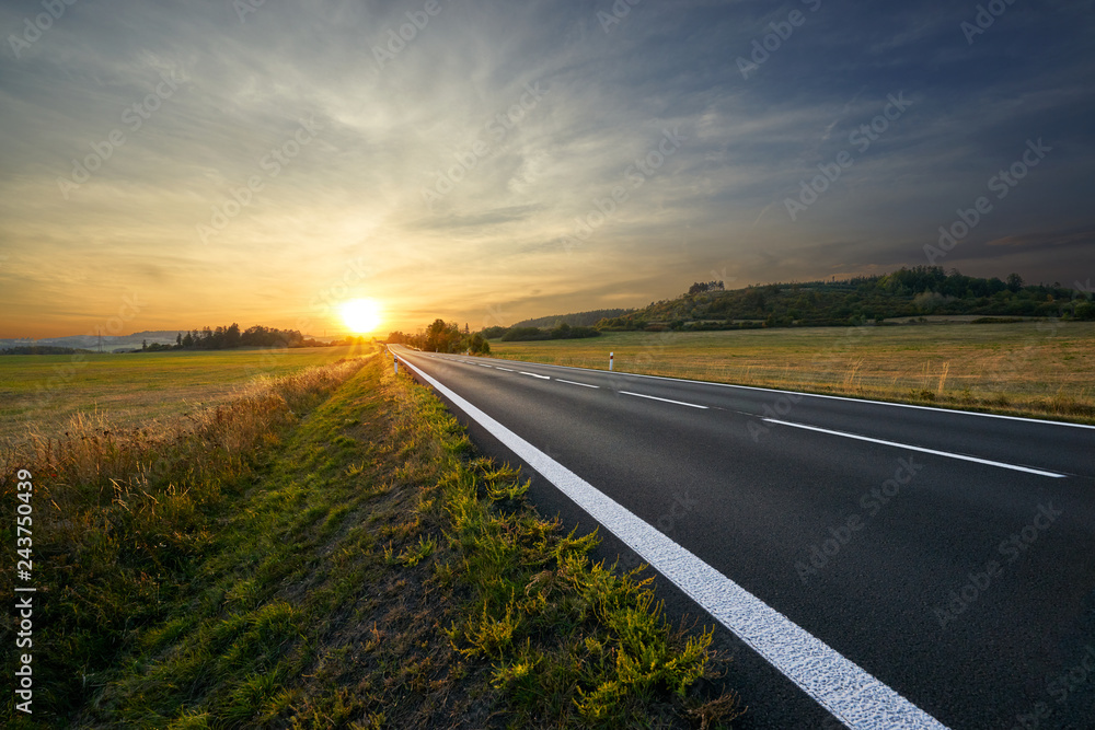 Blank asphalt road running towards sunset in rural countryside