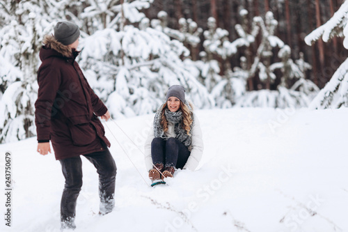 Young couple sledding and enjoying outdoors while falling snow