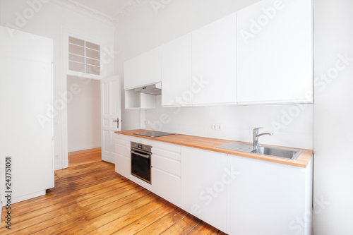 empty, new built-in kitchen with whote furniture and wooden floor