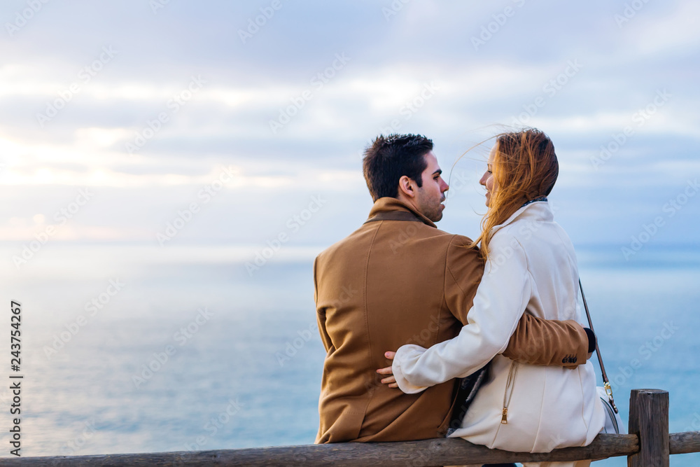 The girl is sitting on a wooden fence and the guy is standing ne The girl is sitting on a wooden fence and the guy is standing ne