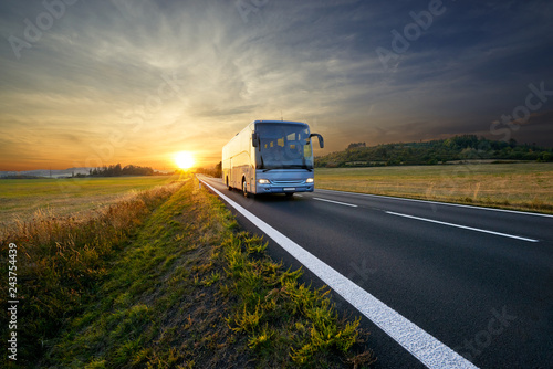 Bus traveling on the asphalt road in rural landscape at sunset