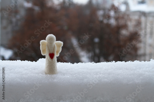 A woolen toy angel stands in the snow on the railing of the balcony against the street. Cloudy winter day