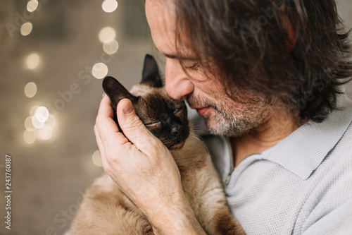 handsome adult man holding a cute, lovely fluffy cat. Siamese breed.