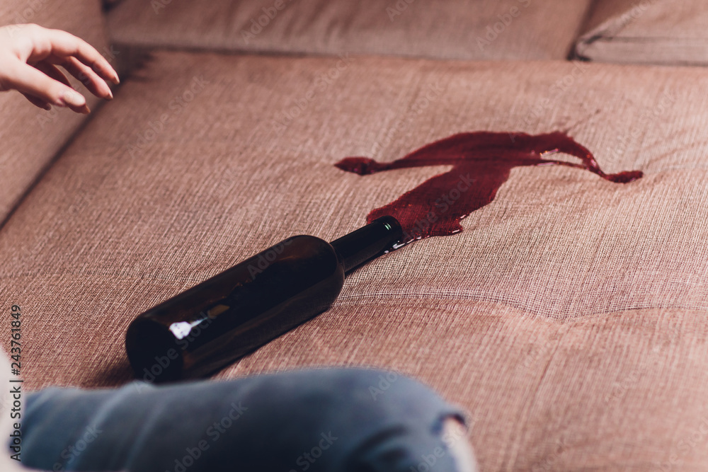 Red wine spilled on a brown couch sofa. dark bottle of red wine dropped - obrazy, fototapety, plakaty 