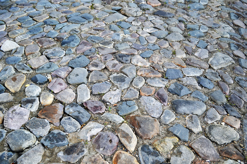 Cobblestone pavement textured pattern of narrow retro street. A fragment of the old town square with a road surface, a typical European urban road material.