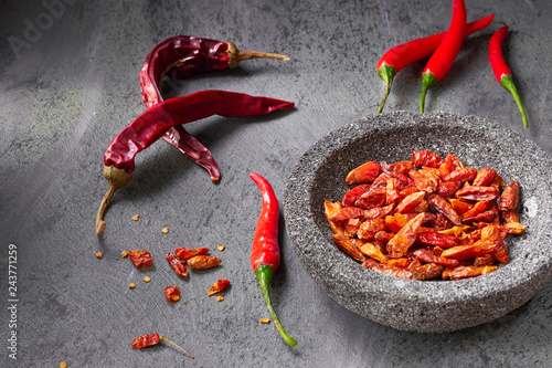 Closeup on  fresh hot chili peppers on dark textured table and dry ones in stone bowl