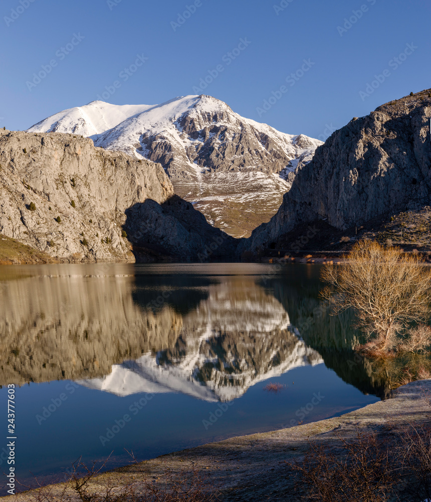 An calm lake reflecting snowy mountains of Leon, Spain on its shores as well as a blue sky above