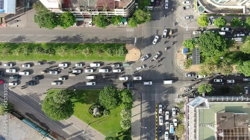 Aerial top down drone view above a busy tree lined triangular traffic intersection in a Southeast Asian city (normal speed variation).