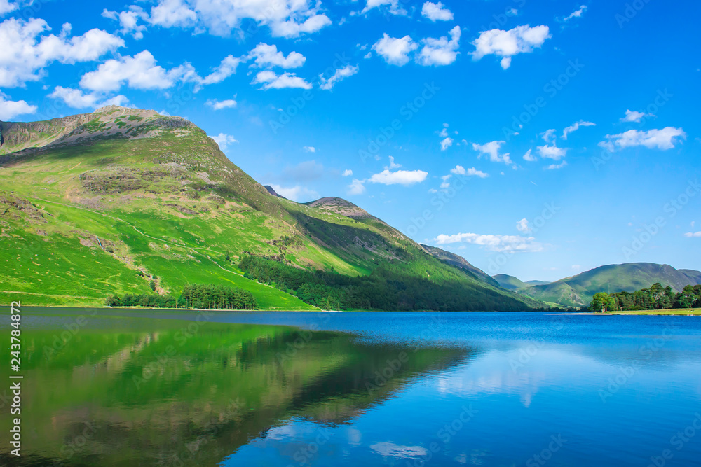 Beauty of british countryside in spring.Green mountain reflecting in crystal clean lake surface and blue sky with few clouds above horizon.
