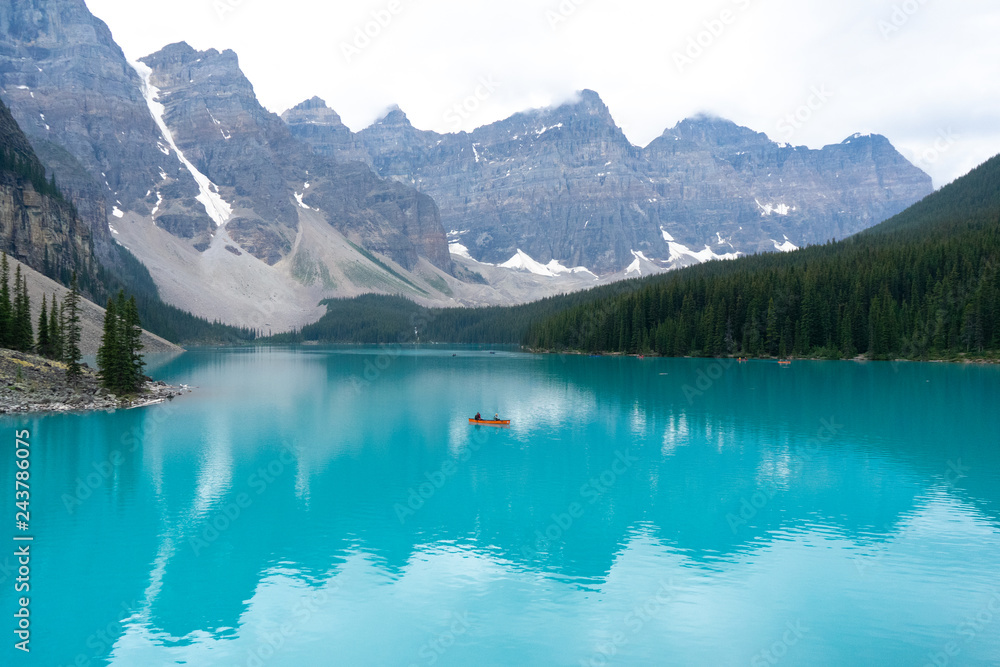 Lone orange canoe on a incredibly teal lake bordered by mountains