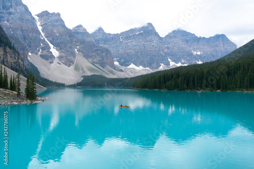 Lone orange canoe on a incredibly teal lake bordered by mountains