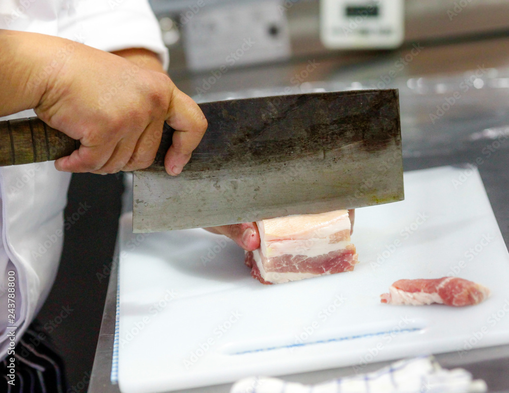 Butcher cuts a piece of meat in kitchen Butcher cuts a piece of meat in kitchen