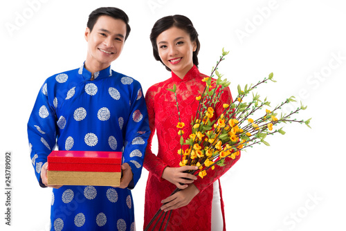 Happy young Asian couple holding traditional Tet symbols: blooming apricot branches and red and golden giftboxes