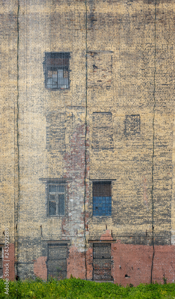 A large mesh covers the old brick wall. The facade of an abandoned building with windows. Weathered dirty dark yellow brickwork with cracks. Grungy surface. Perfect for urban background and design.