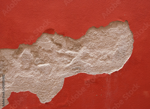New red plaster is flaking off house wall. The Paint layer was not  able to bond with the wall and cause peeling.
