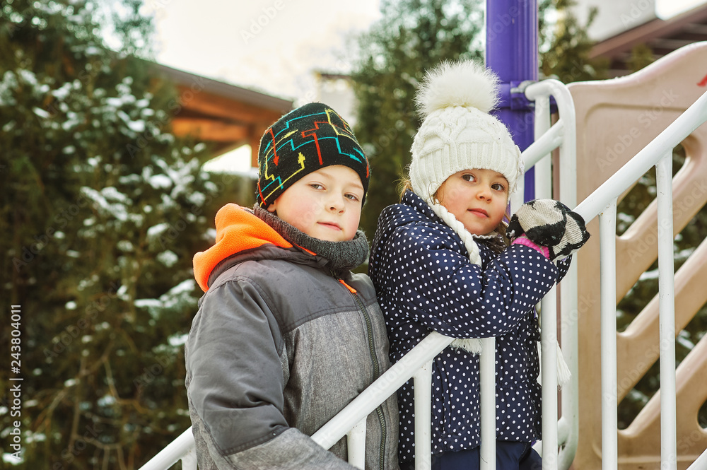 children play in the winter on the Playground, brother and sister in warm jackets and hats for a walk