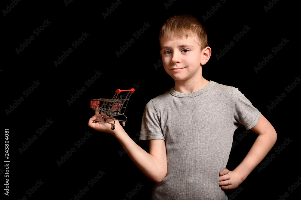 Cute boy holding a small metal shopping trolley in his hands. Isolate on black background. Shopping concept. Copy space. Cute boy holding a small metal shopping trolley in his hands. Isolate on black background. Shopping concept. Copy space.