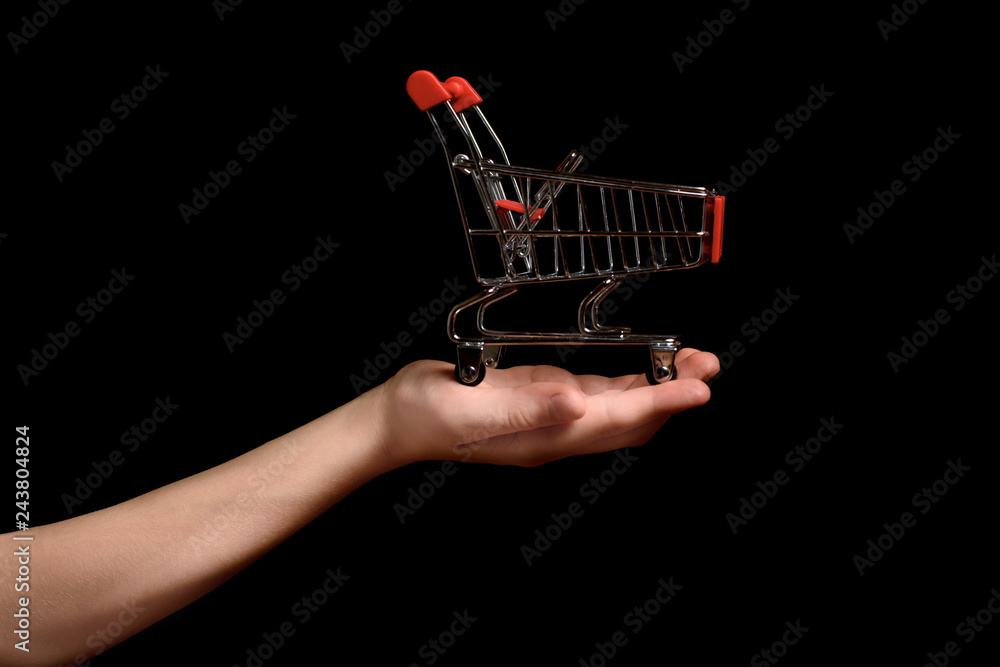 Shopping trolley on a child's palm on a dark background. Shopping concept