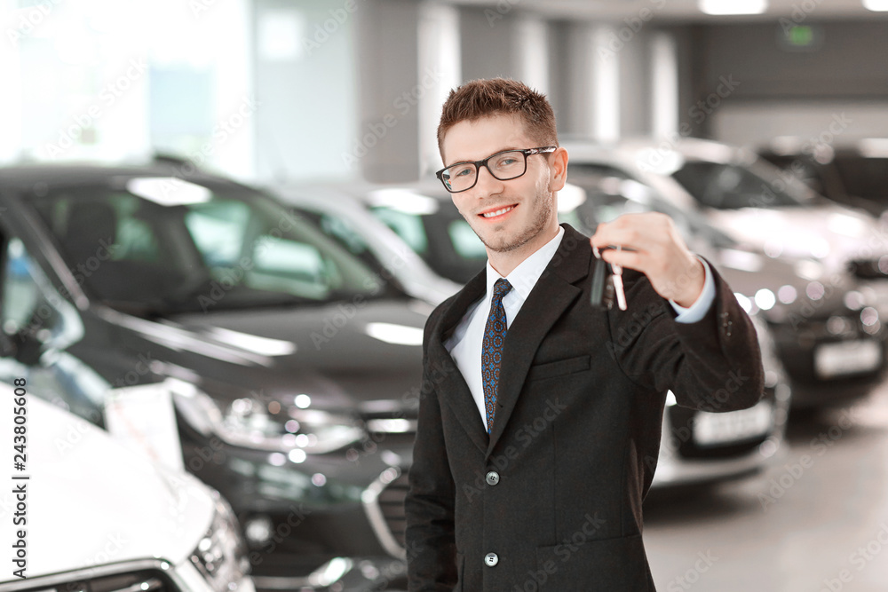 The seller of cars with the keys in hand in the auto showroom. The seller of cars with the keys in hand in the auto showroom.