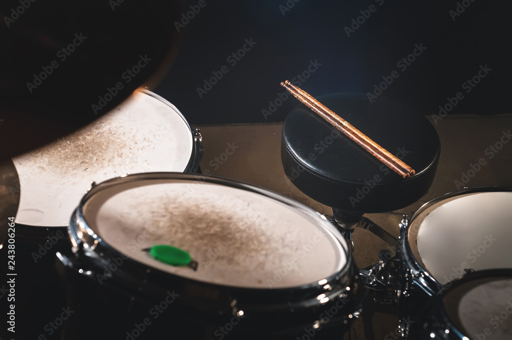 Closeup view of a drum set and Drumsticks in a dark studio. Black drum barrels with chrome trim. The concept of live performances