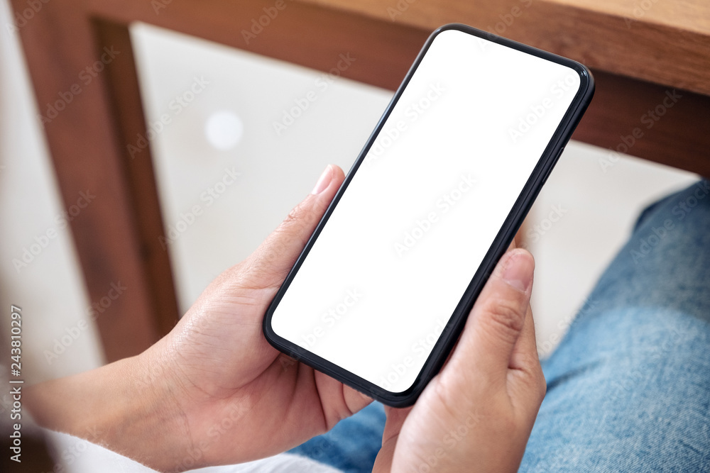 Mockup image of hands holding black mobile phone with blank white screen while sitting Mockup image of hands holding black mobile phone with blank white screen while sitting