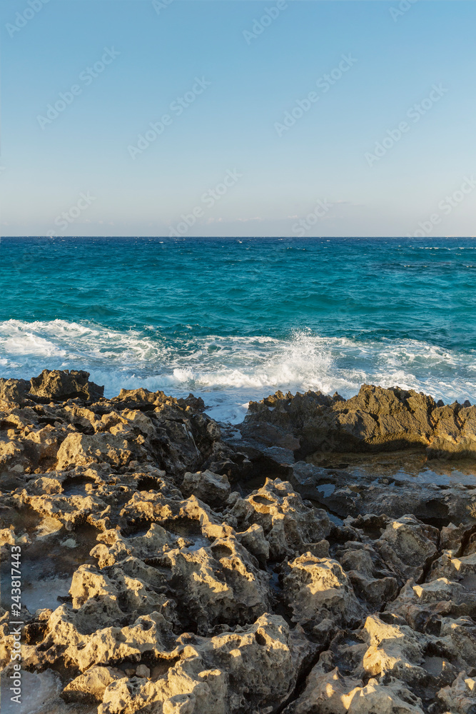 Rocky coast, turquoise sea with foamy water, cloudless sky