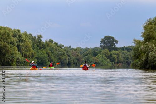 Group of friends (people) travel by kayaks. Kayaking together in wild Danube river and biosphere reserve in summer. Peacefull nature scene of calm river. Water tourism concept.