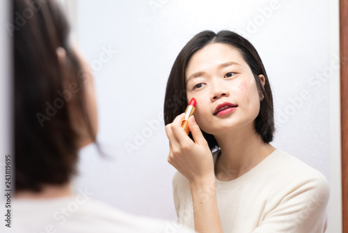 asian female applying makeup and looking in mirror