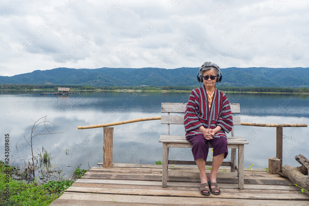 An Elderly woman wearing sunglasses sitting side the lake.