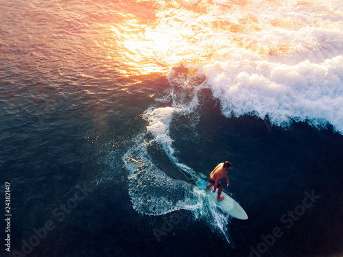 Aerial view of the young man surfing the wave at sunset