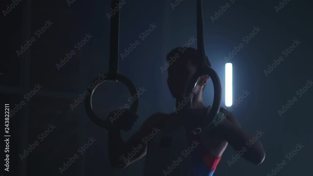 Gymnast on a dark background stands on his hands using rings in the air
