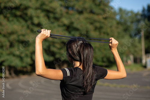 Young sporty tanned girl stretching with a jump rope at the stadium. Outdoor shot with sun light