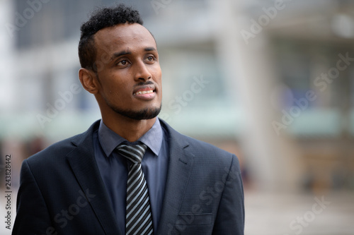 Happy young African businessman thinking and looking up outdoors