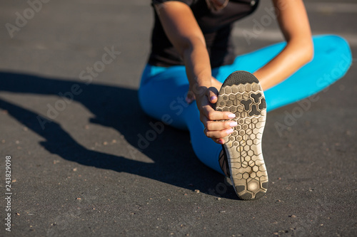 Closeup shot of athletic girl stretching before workout at the stadium. Space for text