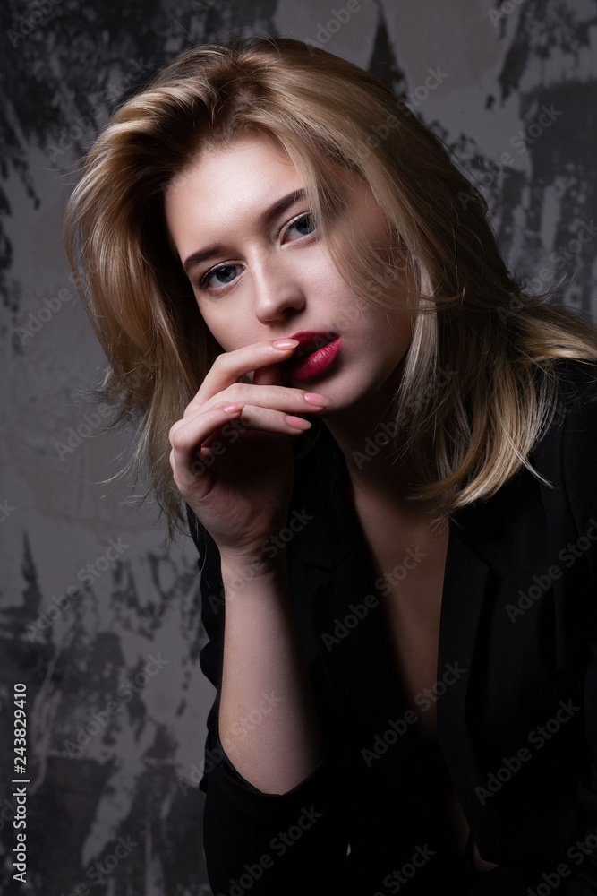 Elegant blonde woman with perfect skin wearing black jacket posing at studio with shadows Elegant blonde woman with perfect skin wearing black jacket posing at studio with shadows