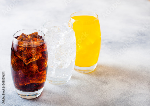 Glasses of soda drink with ice cubes and bubbles on stone kitchen table background. Cola and orange lemonade soda photo