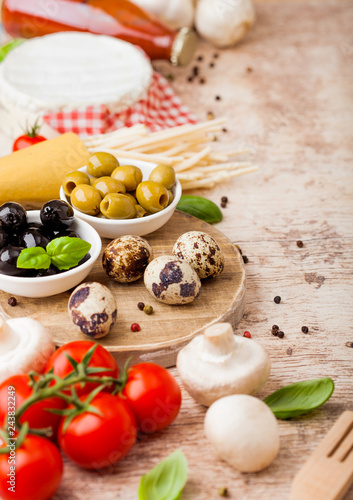 Homemade spaghetti pasta with quail eggs with bottle of tomato sauce and cheese on wooden background. Classic italian village food. Garlic, champignons, black and green olives, oil and spatula.