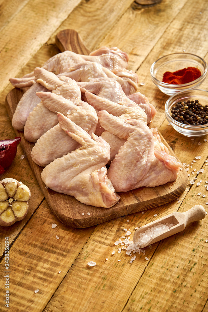 Fresh organic chicken wings on a chopping board with spices and vegetables on wooden table.