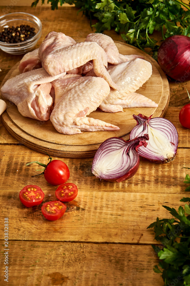 Fresh organic chicken wings on a chopping board with spices and vegetables on wooden table. Fresh organic chicken wings on a chopping board with spices and vegetables on wooden table.