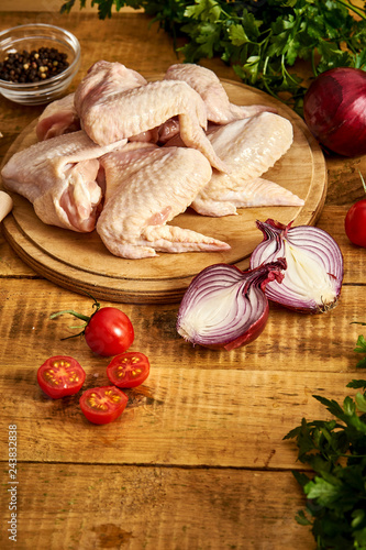 Obraz na płótnie Fresh organic chicken wings on a chopping board with spices and vegetables on wooden table. w salonie