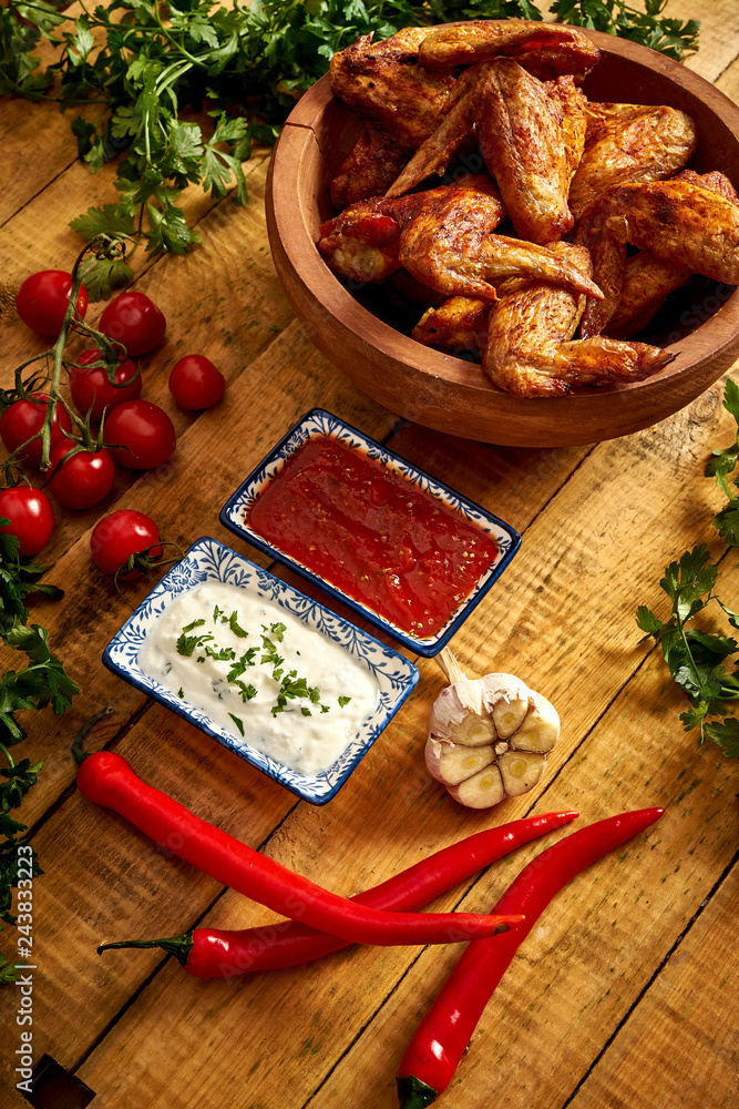 Delicious grilled chicken wings in bowl with spices and vegetables with dips on wooden table.