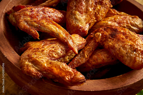 Close up of delicious grilled chicken wings in wooden bowl on wooden table.